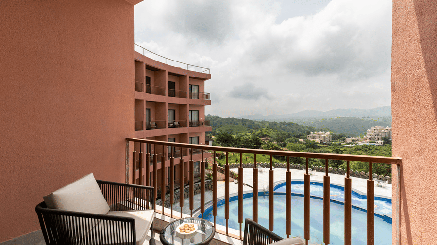 A private balcony at Osian Valley Resort & Spa, Kumbhalgarh, overlooking the green valley and mountains, with a cosy seating arrangement ideal for morning tea or sunset views.