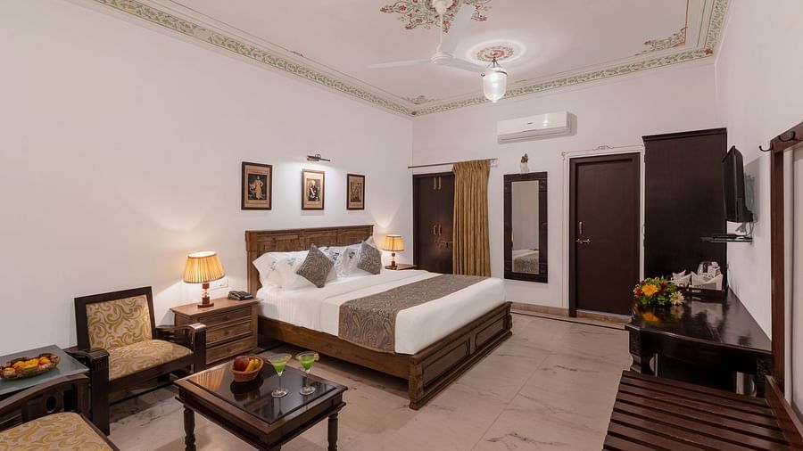 A spacious bedroom at Panna Vilas Palace, featuring a wooden table, cushioned furniture, and warm lighting | Panna Vilas Udaipur