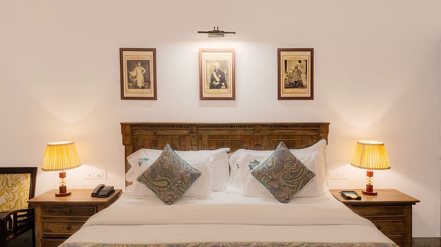 A spacious bed with wooden bedside tables on each side, both featuring lamps, and a photo frame above the headboard at Panna Vilas Palace