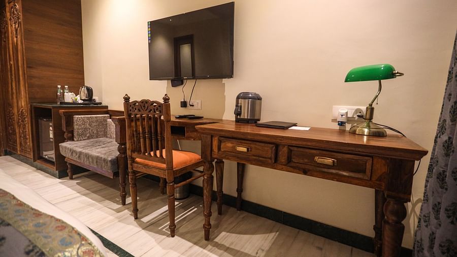 Spacious room with a wooden table and chairs, a wall-mounted television, and essential items on the table | Panna Vilas Udaipur
