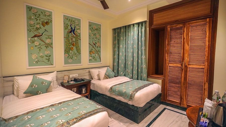 Diagonal view of the spacious room with twin beds placed side by side, a wooden bedside table in the middle, three photo frames above the headboard, and wooden storage | Panna Vilas Udaipur