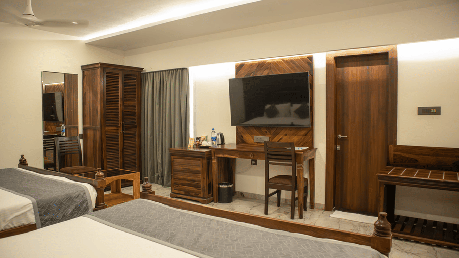 A detailed view of a cosy bedroom featuring a cabinet, a wall-mounted television, a wooden wardrobe, and an opening to another room at Papaya Tree Hotels Club Room.