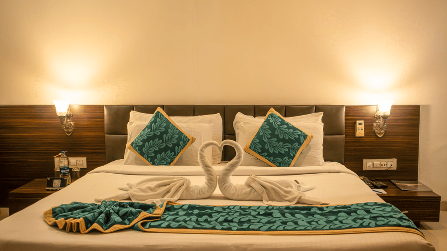 Deluxe Room of Papaya Tree Hotels with a double bed draped with elegant linen and swan decor, 2 side table and 2 overhead lamps glowing.