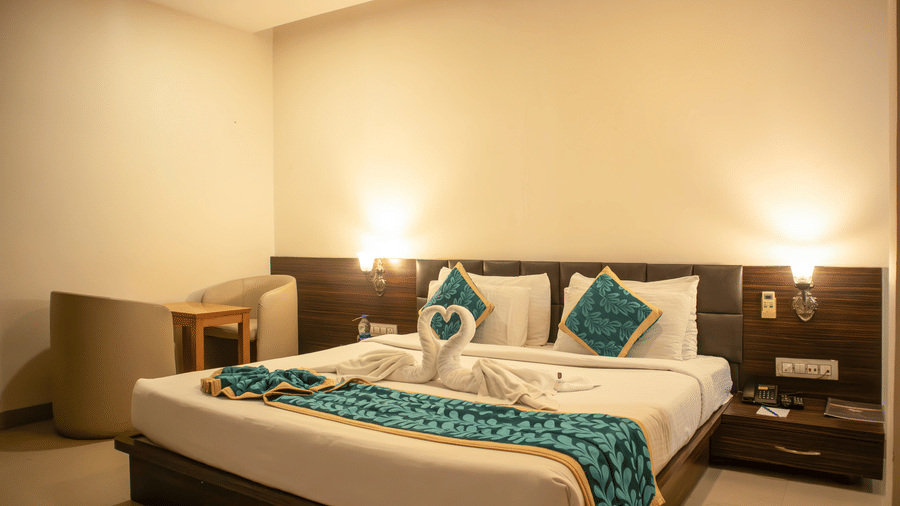 Deluxe Room of Papaya Tree Hotels furnished with double bed, a small lounge area with 2 armchairs and a coffee table, and 2 overhead lamps glowing.