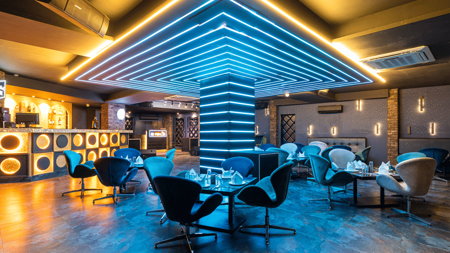 Modern lounge area of Re-Pub-Liq, Papaya Tree Hotels, featuring sleek furniture, a central column with illuminated ceiling panels, and an inviting bar setup.