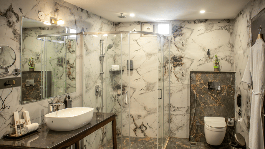 A well-structured bathroom featuring a sink on a marble counter-top, a large mirror with a spacious shower cubicle at a Suite of Papaya Tree Hotels.