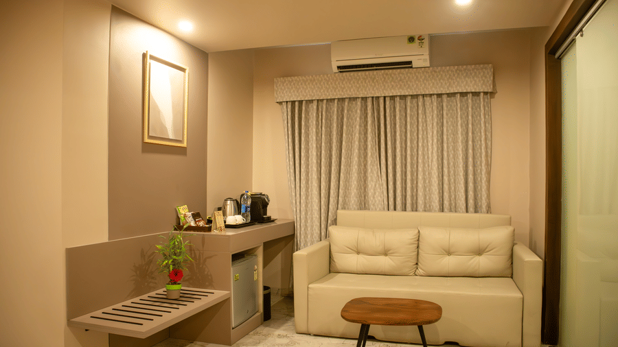 Living room of a Suite at Papaya Tree Hotels having a 2-seating sofa, carpet flooring, a centre table, and large curtains draped over the window.