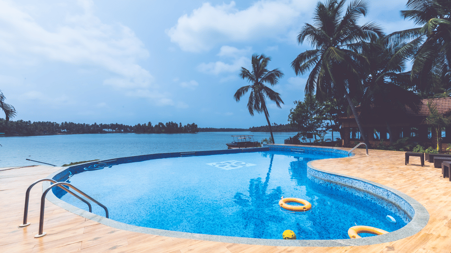 Swimming pool with pool floats, surrounded by palm trees and open sky at Paradise lagoon Resort, Udupi.