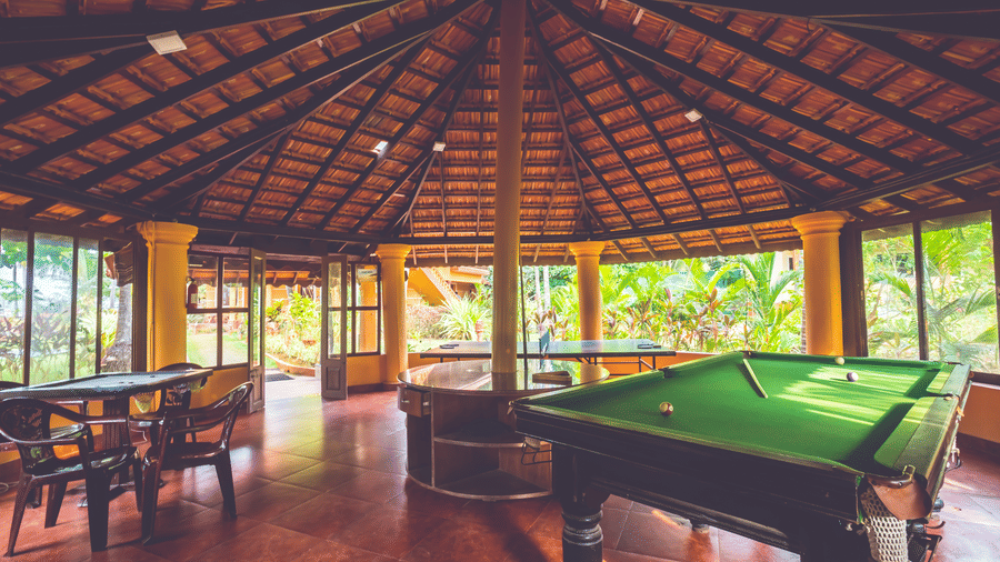 Open-sided hut with a tiled roof, containing a green snooker table and wooden seating at Paradise Lagoon Resort, Udupi.
