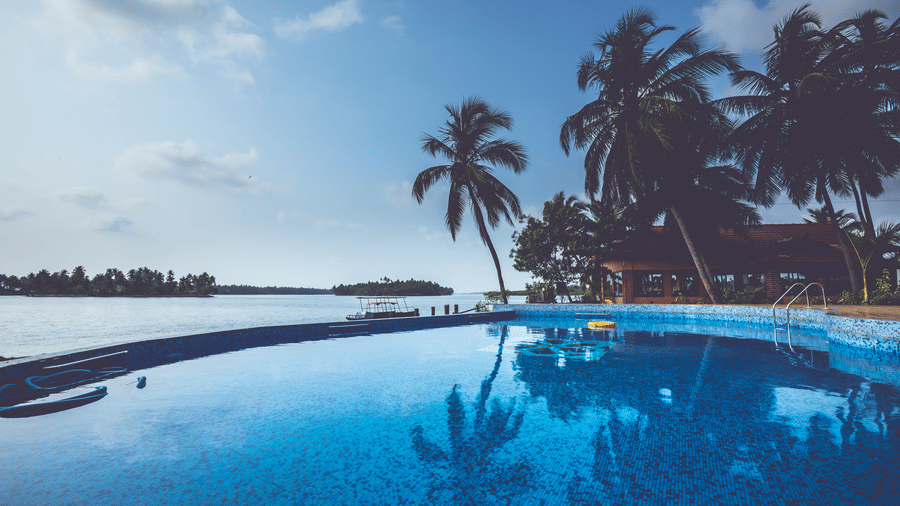 Infinity swimming pool with palm trees along the edge, overlooking water and distant greenery at Paradise Lagoon Resort, Udupi.