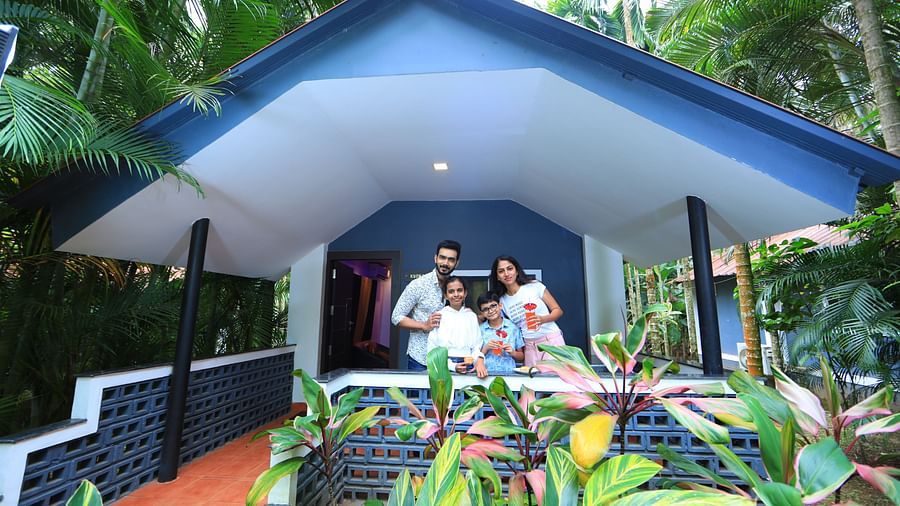 Facade of an accommodation with three people standing in front of it, posing for a photo at Parampara Resort & Spa, Kushalnagar.