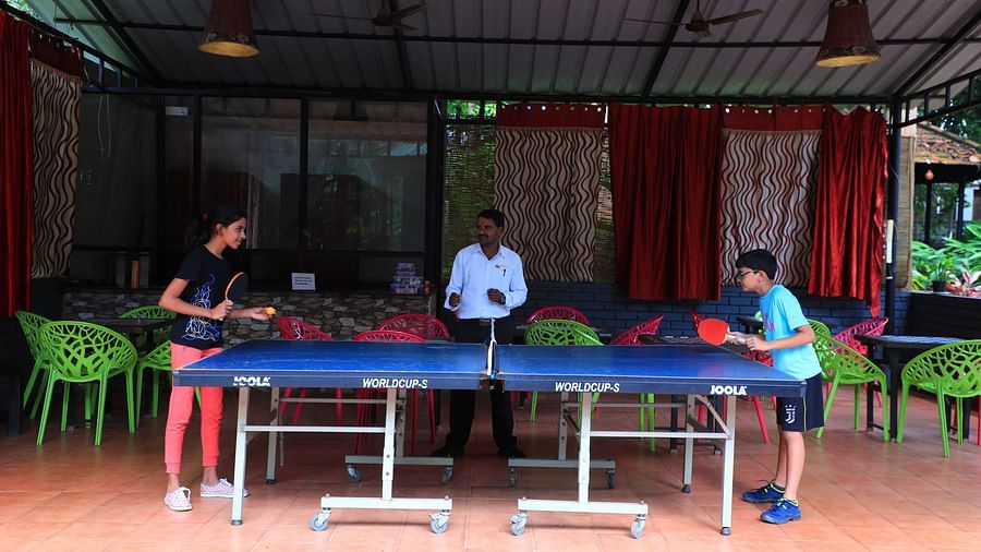 Image of two people playing table tennis and a man watching them at Parampara Resort & Spa, Kushalnagar.
