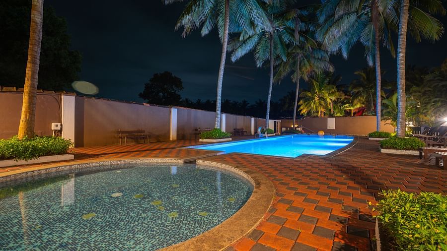 Night view of the swimming pool at Parampara Resort & Spa, Kushalnagar surrounded by trees.
