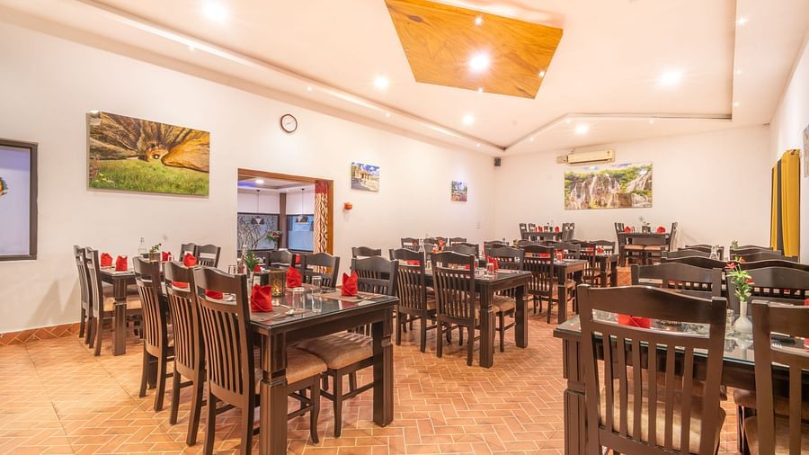Image of an indoor dining area with wooden tables and chairs at Parampara Resort & Spa, Kushalnagar.