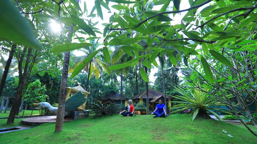 Wide angle shot of two people holding a yoga pose amidst greenery at Parampara Resort & Spa, Kushalnagar.