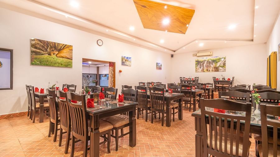 An indoor dining area with wooden tables and chairs at Parampara Resort & Spa, Kushalnagar.