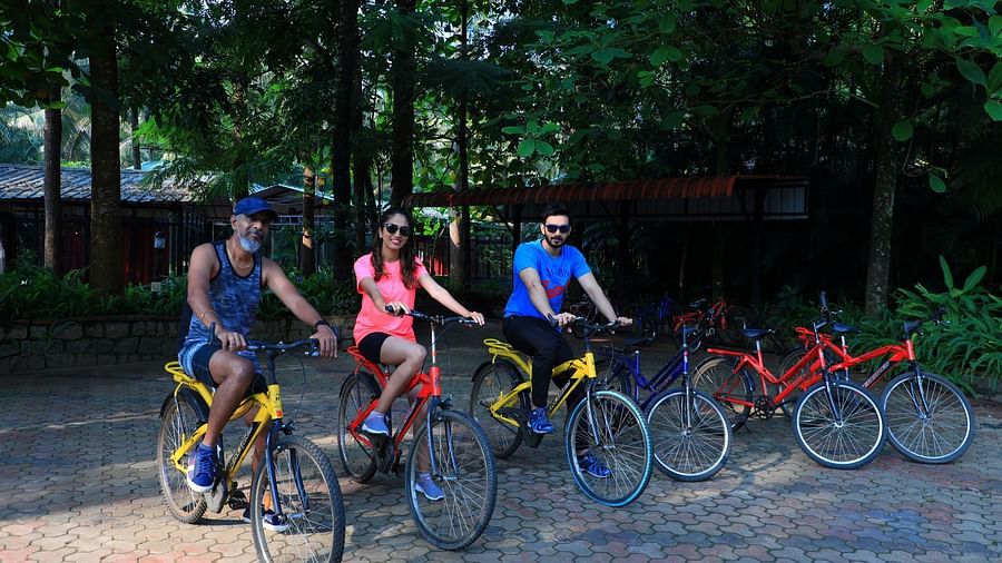 Three people on a cycle with trees in the background at Parampara Resort & Spa, Kushalnagar.