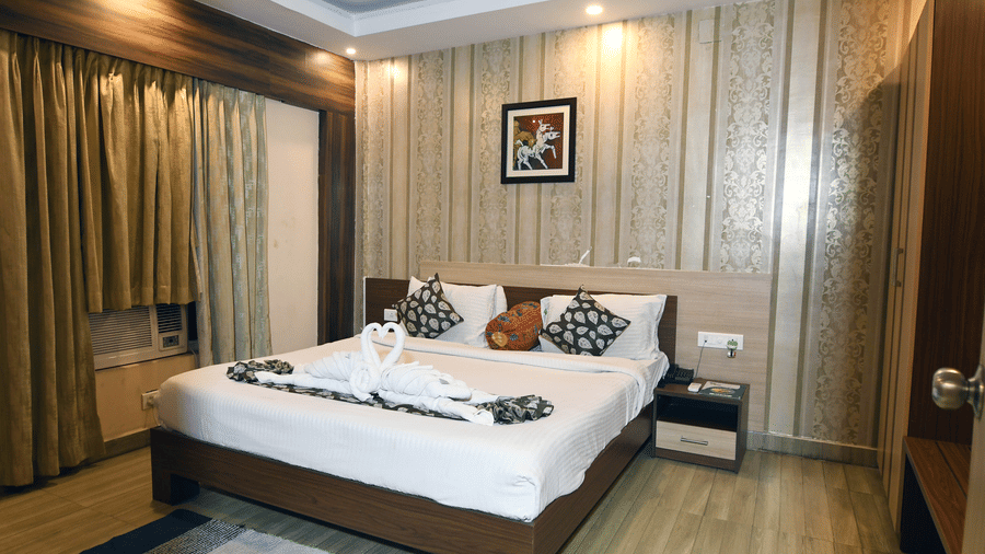 A room with a kind size bed with wooden panelling behind it featuring swan towel decoration, curtains, and a wall art at Pipul Hotel And Resort, Puri.