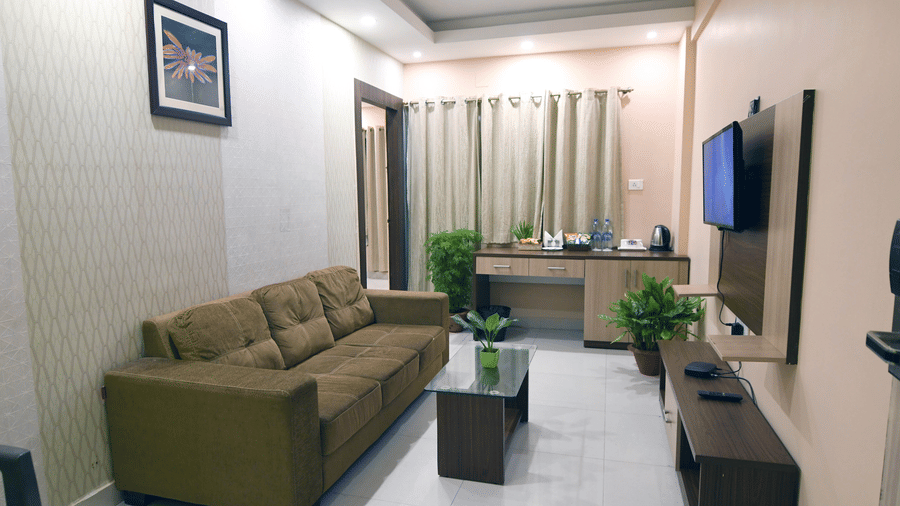 A cosy living area of a Suite at Pipul Hotel And Resort, Puri, featuring a sofa, a glass coffee table, and a wall-mounted TV.