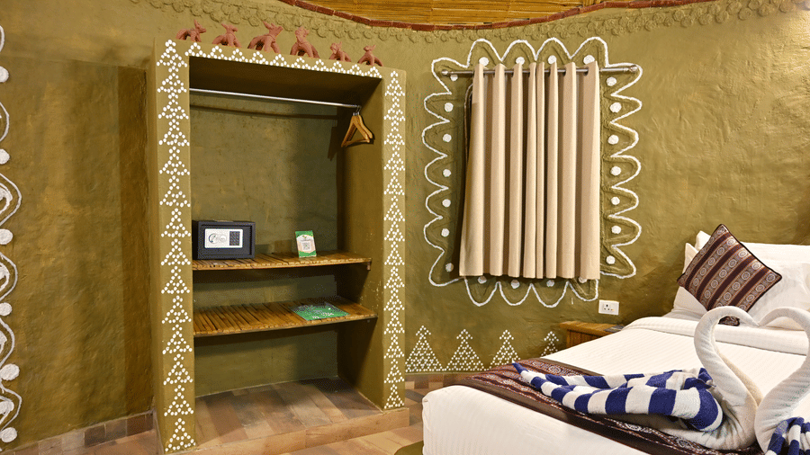 Tribal cottage interior with hand-painted tribal wall art, a wooden shelf unit, a bed dressed in patterned linen and long curtains close by.