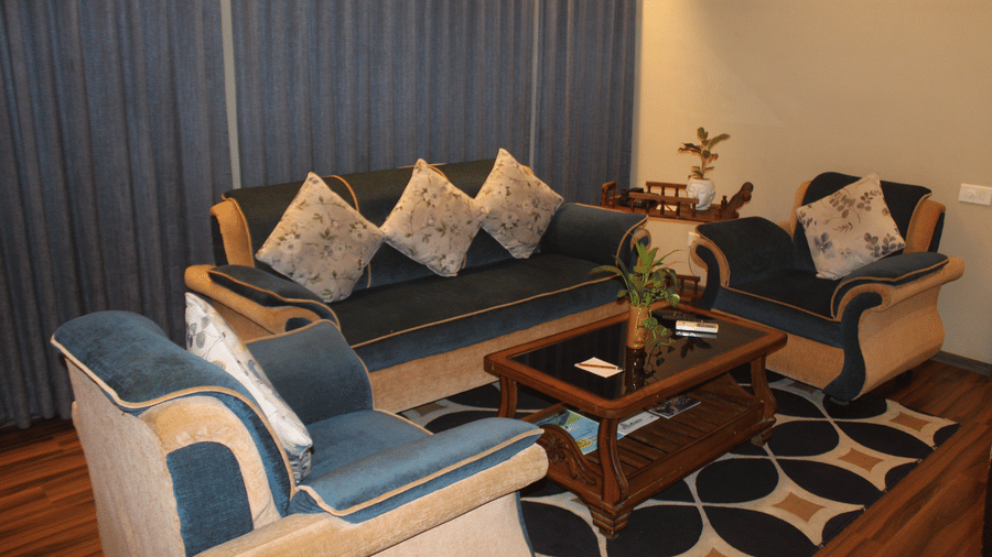 Sitting area with plush blue sofas, patterned rug, indoor plant, and full curtains at Pipul Padmaja Premium Hotel & Convention.