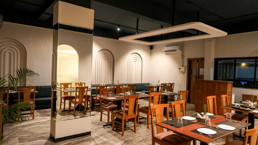  An interior view of the bright dining hall with white walls, wooden chairs, and recessed archways at Pravasa Hotel, Kolhapur.