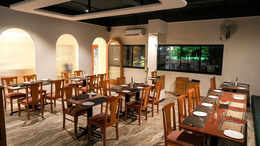 A well-appointed indoor dining room with wooden tables and chairs, white walls, and elegant archways at Pravasa Hotel, Kolhapur.