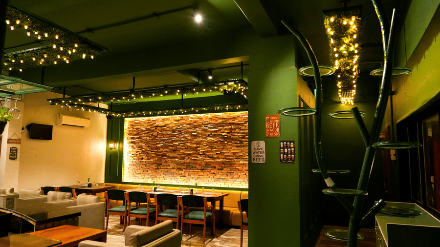 A vibrant lounge area with striking green walls, comfy seating, and a feature wall of exposed brick at Pravasa Hotel, Kolhapur.