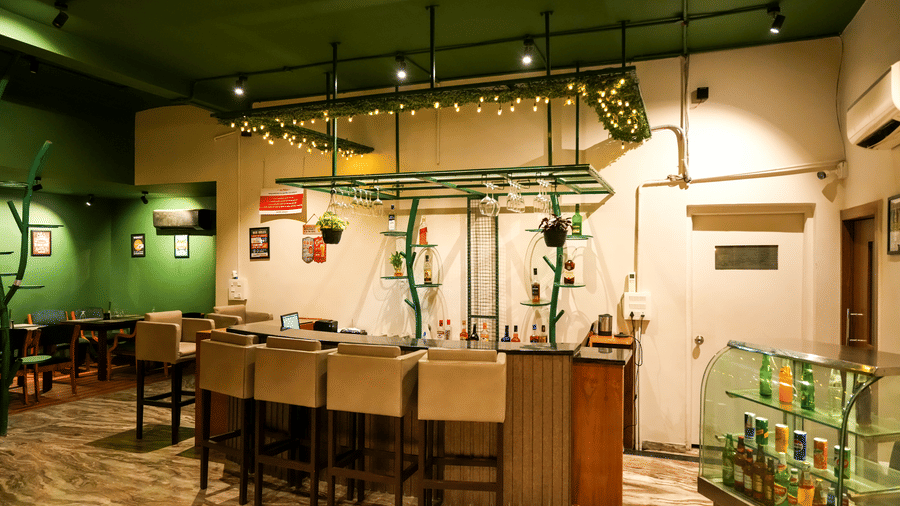  A well-lit service bar with high stools and a glass display case for drinks in the casual dining area of Pravasa Hotel, Kolhapur.