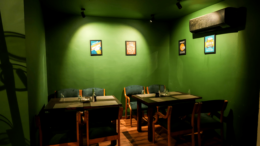  A private or cosy dining room with dark tables, green walls, and framed artwork at Pravasa Hotel, Kolhapur.