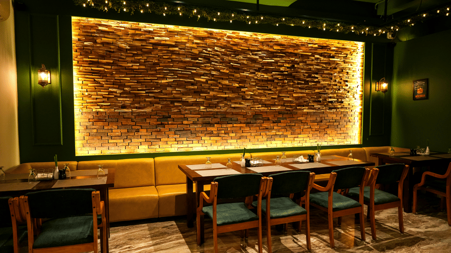  A warm dining section with a long yellow upholstered booth and a dramatic backlit stone feature wall at Pravasa Hotel, Kolhapur.