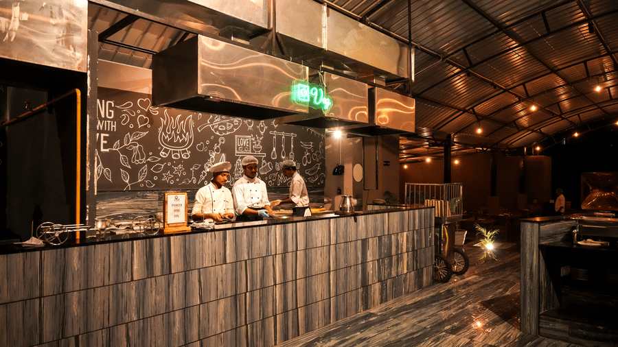  Chefs are busy working behind a modern, textured counter in the open kitchen area of Pravasa Hotel, Kolhapur.
