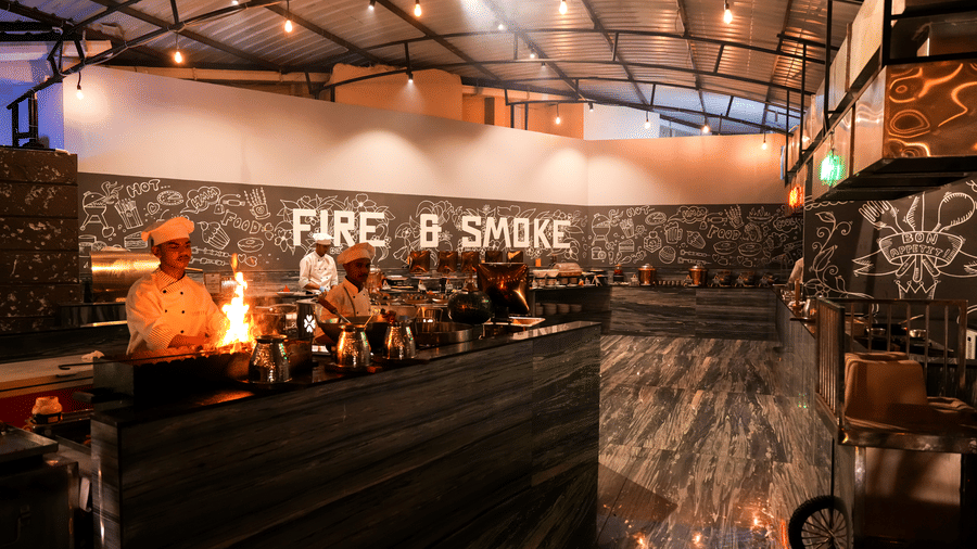 Chefs cooking in open kitchen area with visible flames at Pravasa Hotel, Kolhapur.