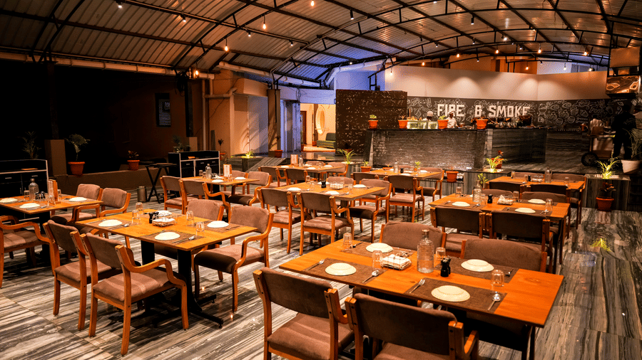 Dining area with tables and chairs under indoor lighting at Pravasa Hotel, Kolhapur.