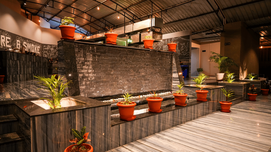 A stylish indoor seating area with plants in terracotta pots and a corrugated iron roof at Pravasa Hotel, Kolhapur. 