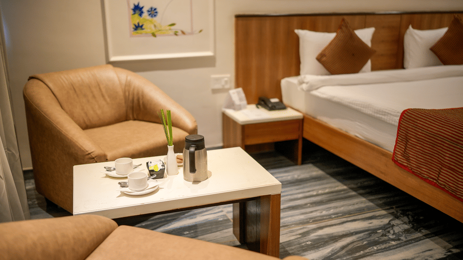  A view of the deluxe room's seating area and bed, featuring modern artwork and tan armchairs at Pravasa Hotel, Kolhapur.