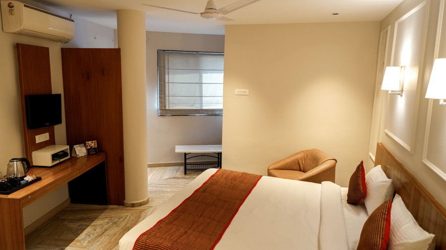  A well-equipped guest room with a wooden desk, a kettle, and a separate sitting area near a window at Pravasa Hotel, Kolhapur. 