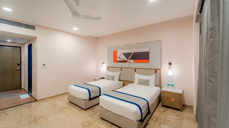 Twin beds with white and blue bedding in a well-lit hotel room | Superior Room | Pravasa Hotel, Vijayapura