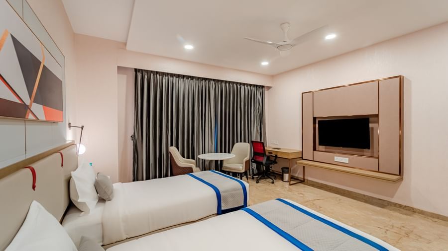 Corner of a hotel room featuring twin beds and a wall-mounted TV | Superior Room | Pravasa Hotel, Vijayapura