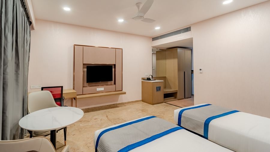A hotel room featuring twin beds and a wall-mounted TV | Superior Room | Pravasa Hotel, Vijayapura
