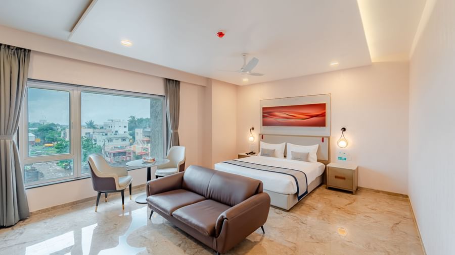  A spacious room with a king-size bed, a sofa, and a city view | Studio Suite | Pravasa Hotel, Vijayapura