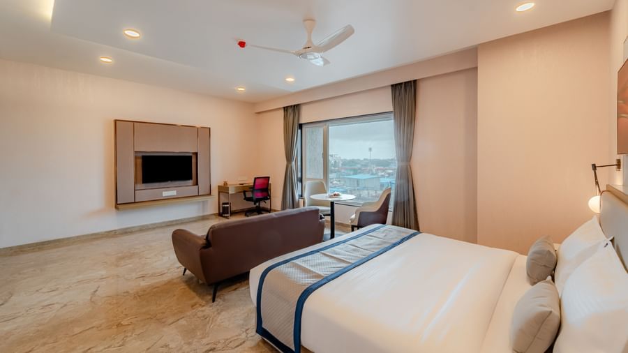  A spacious room with a king-size bed, a sofa, and a wall-mounted television | Studio Suite | Pravasa Hotel, Vijayapura