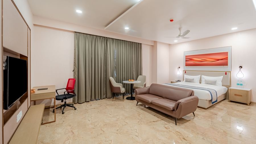Spacious room with a king-size bed, a sofa, and a wall-mounted television | Studio Suite | Pravasa Hotel, Vijayapura