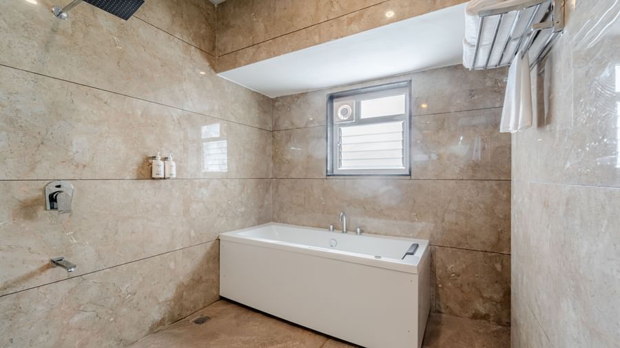 A suite bathroom with a white bathtub and patterned beige tiles | Suite | Pravasa Hotel, Vijayapura