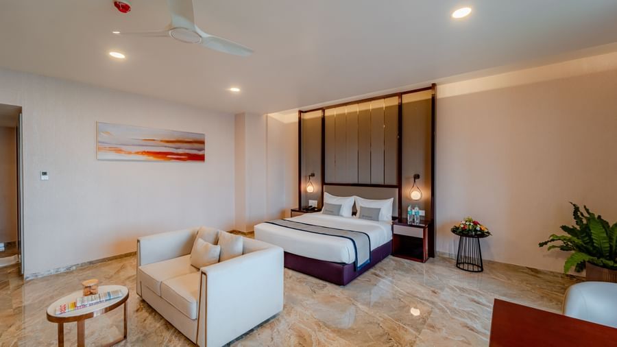 Bright and elegant suite with a bed, living space, and a dining setup | Suite | Pravasa Hotel, Vijayapura