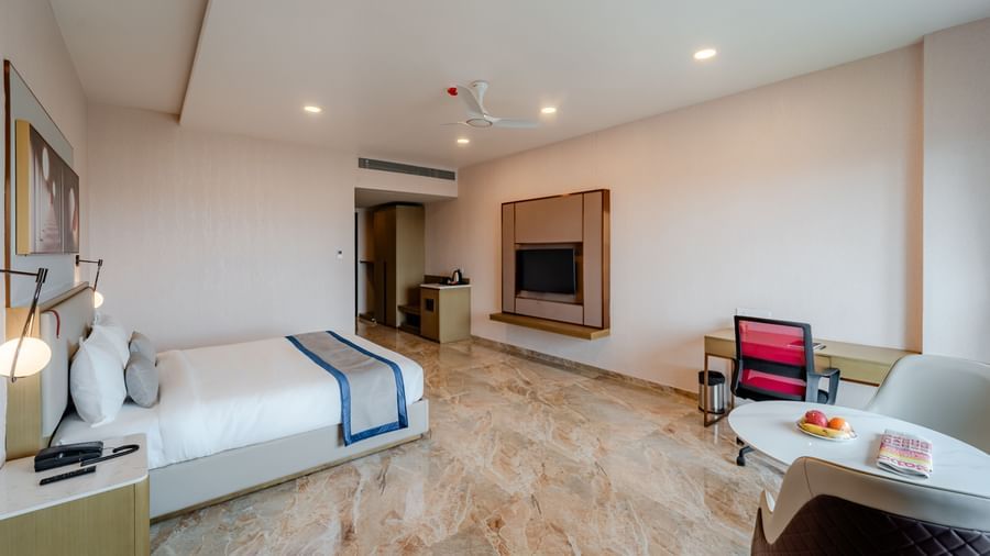  A hotel bedroom with a large bed, TV, and a desk, well-lit | Premium Room | Pravasa Hotel, Vijayapura