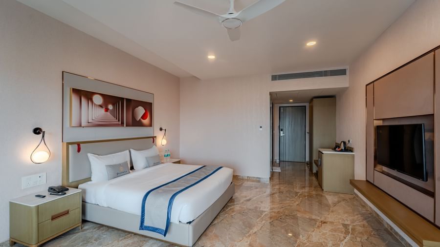 Hotel bedroom featuring a king bed, bedside tables, and a large window | Premium Room | Pravasa Hotel, Vijayapura