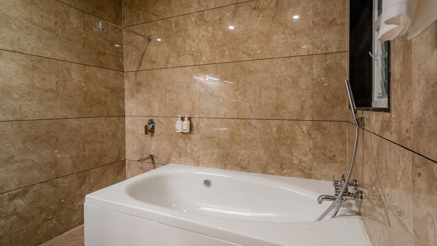 Modern bathroom with a clean white bathtub and marble-patterned tiles | Premium Room | Pravasa Hotel, Vijayapura