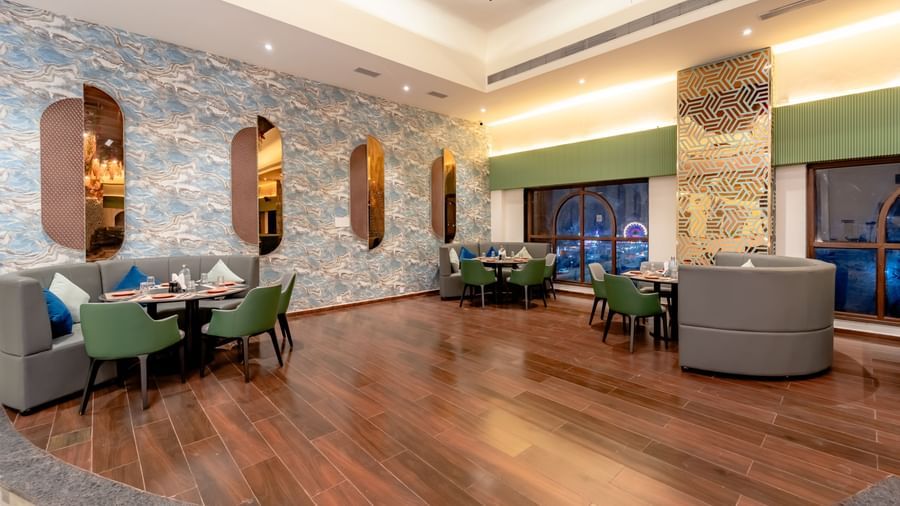 The hotel dining area with green booths and bright orange chairs | Pravasa Hotel, Vijayapura