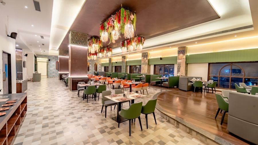 The restaurant with orange and green seating and intricate ceiling decorations | Pravasa Hotel, Vijayapura
